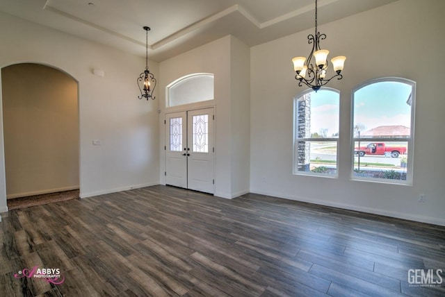foyer entrance with a chandelier, dark wood-type flooring, a raised ceiling, arched walkways, and baseboards