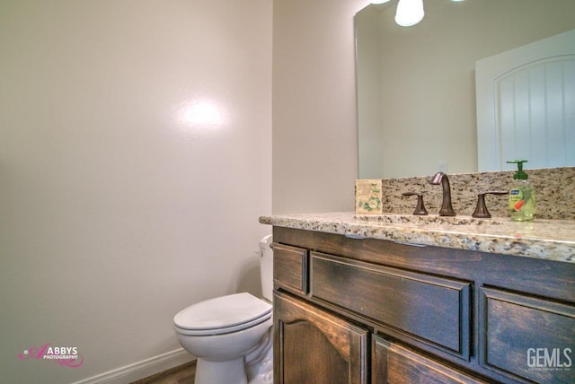 half bath featuring toilet, vanity, baseboards, and wood finished floors