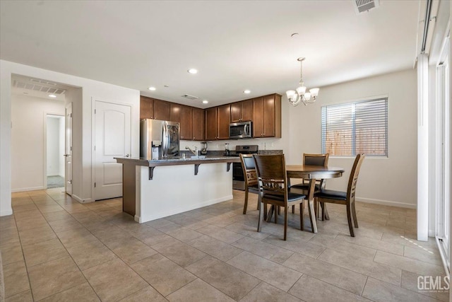 kitchen with appliances with stainless steel finishes, a kitchen breakfast bar, decorative light fixtures, a center island with sink, and a chandelier