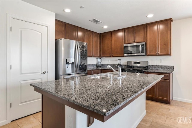 kitchen featuring a center island with sink, sink, stainless steel appliances, and dark stone counters