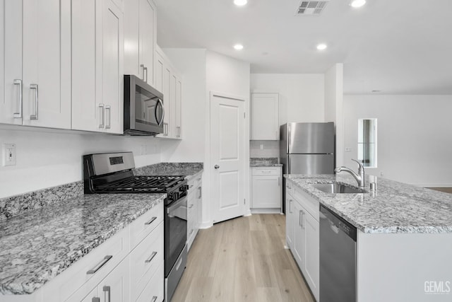 kitchen with stainless steel appliances, sink, white cabinetry, light hardwood / wood-style flooring, and a center island with sink