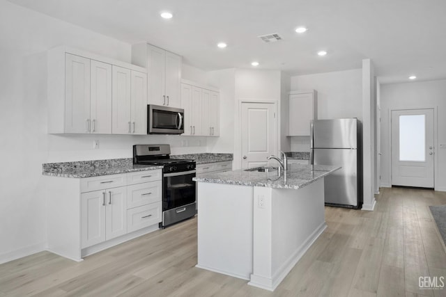 kitchen with a kitchen island with sink, appliances with stainless steel finishes, light stone countertops, sink, and white cabinetry