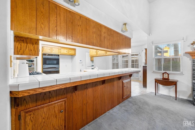 kitchen featuring dobule oven black, light colored carpet, brown cabinets, a peninsula, and light tile patterned flooring