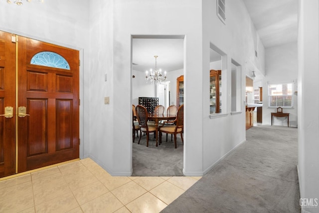 foyer entrance featuring carpet, visible vents, a towering ceiling, an inviting chandelier, and tile patterned floors