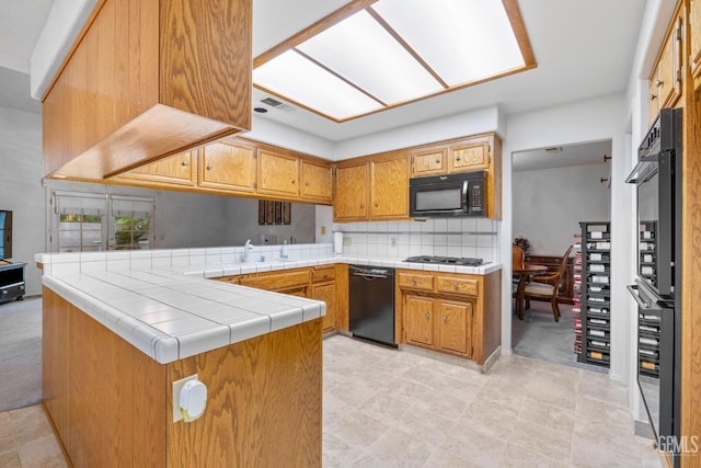 kitchen featuring a peninsula, black appliances, brown cabinetry, and backsplash