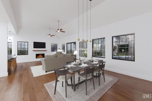 dining space with high vaulted ceiling, a warm lit fireplace, baseboards, and hardwood / wood-style flooring