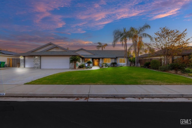 view of front of home featuring a lawn, concrete driveway, stone siding, an attached garage, and fence