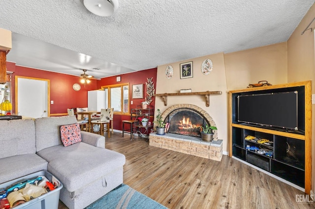 living room with hardwood / wood-style flooring, ceiling fan, a brick fireplace, and a textured ceiling