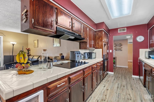 kitchen with tile countertops, stainless steel appliances, and light wood-type flooring