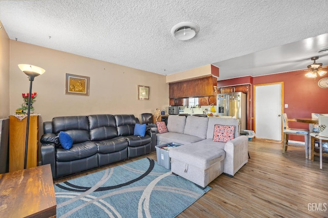 living room featuring ceiling fan, light hardwood / wood-style flooring, and a textured ceiling