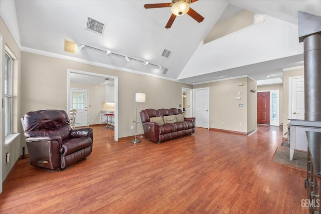 living room featuring ceiling fan, high vaulted ceiling, wood-type flooring, ornamental molding, and a wood stove