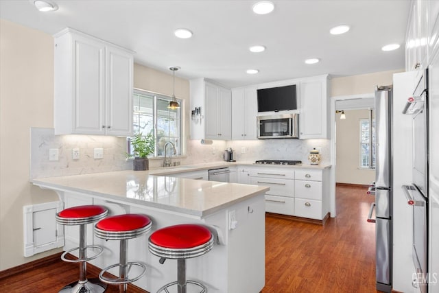 kitchen featuring stainless steel appliances, decorative light fixtures, kitchen peninsula, and white cabinets