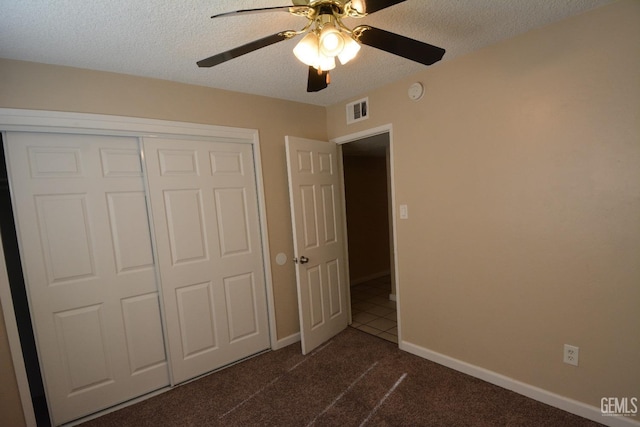 unfurnished bedroom with ceiling fan, dark carpet, a closet, and a textured ceiling