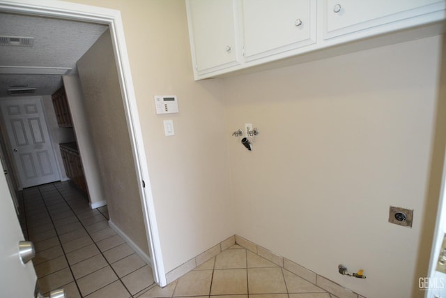 clothes washing area featuring light tile patterned flooring, gas dryer hookup, cabinets, a textured ceiling, and hookup for an electric dryer