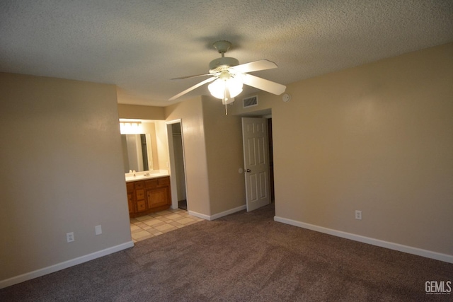 unfurnished bedroom with ceiling fan, light colored carpet, ensuite bathroom, and a textured ceiling