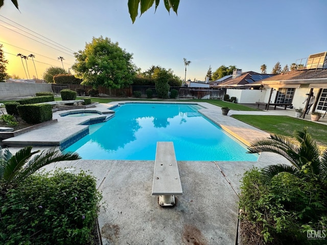pool at dusk featuring an in ground hot tub, a diving board, a patio area, a fenced in pool, and a fenced backyard