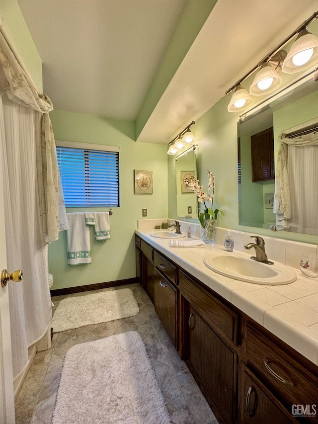 bathroom with a sink, baseboards, toilet, and double vanity