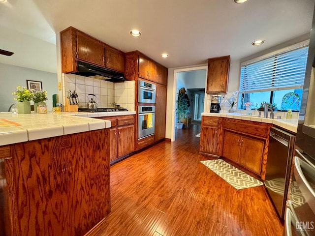 kitchen with under cabinet range hood, tile countertops, wood finished floors, and backsplash