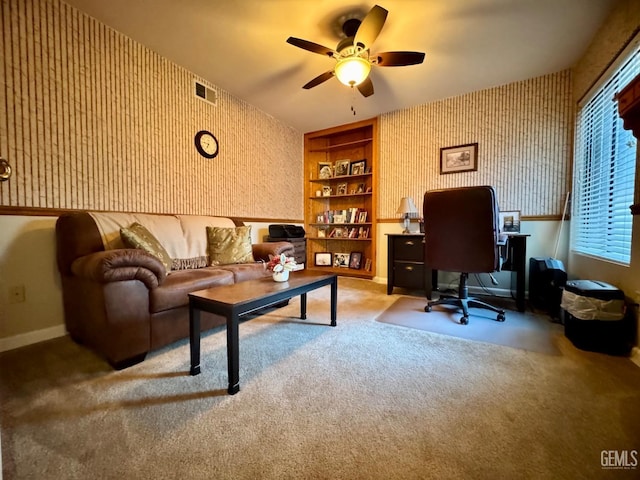 carpeted office space with built in shelves, a ceiling fan, wallpapered walls, baseboards, and visible vents