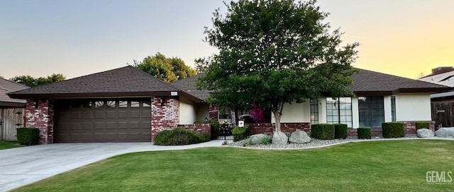 single story home featuring driveway, roof with shingles, brick siding, a yard, and an attached garage