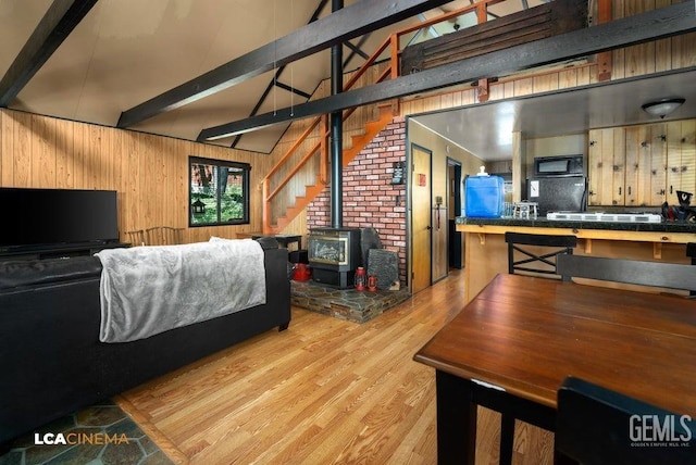 bedroom with beamed ceiling, wooden walls, light hardwood / wood-style floors, and a wood stove