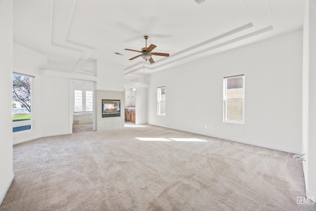 unfurnished living room featuring a tray ceiling, visible vents, a fireplace, and light carpet