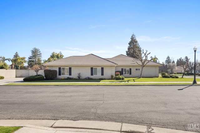 ranch-style house with stucco siding, fence, a front lawn, and a tiled roof