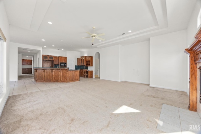 unfurnished living room with arched walkways, ceiling fan, a tiled fireplace, and light carpet