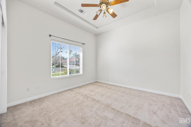 spare room with a raised ceiling, visible vents, a ceiling fan, light carpet, and baseboards