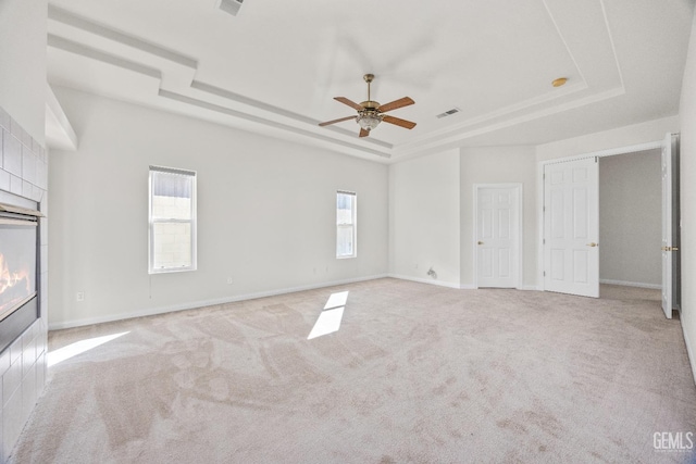 unfurnished room with light colored carpet, a raised ceiling, visible vents, and a tiled fireplace