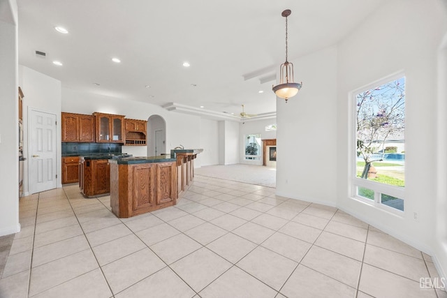 kitchen featuring hanging light fixtures, a center island, brown cabinetry, dark countertops, and a glass covered fireplace