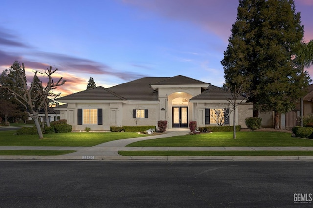 view of front facade with stucco siding, a front lawn, and french doors