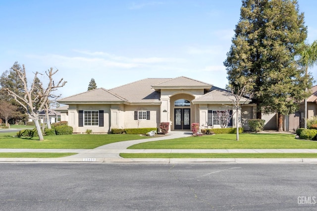 view of front of property featuring french doors, a tile roof, a front lawn, and stucco siding