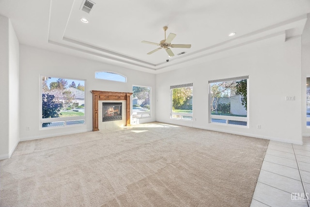 unfurnished living room with ceiling fan, light colored carpet, visible vents, a tiled fireplace, and a raised ceiling