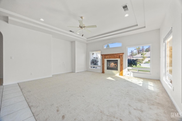 unfurnished living room featuring a tray ceiling, visible vents, light carpet, and a tile fireplace