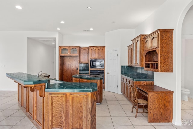 kitchen with a kitchen island, built in microwave, open shelves, brown cabinetry, and glass insert cabinets