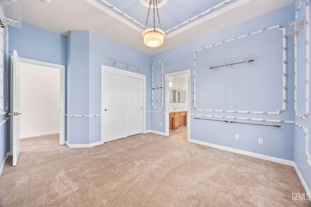 unfurnished bedroom featuring a tray ceiling, a closet, ensuite bathroom, light carpet, and baseboards