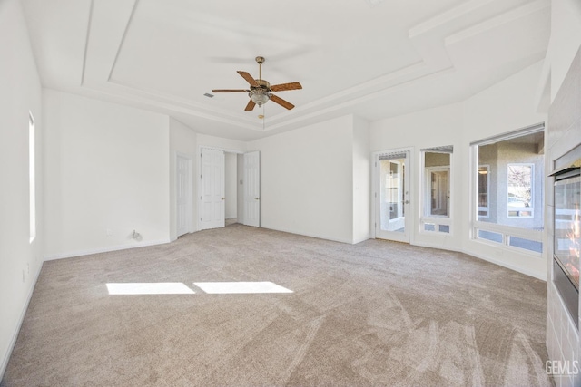 unfurnished bedroom with light carpet, a raised ceiling, and a ceiling fan