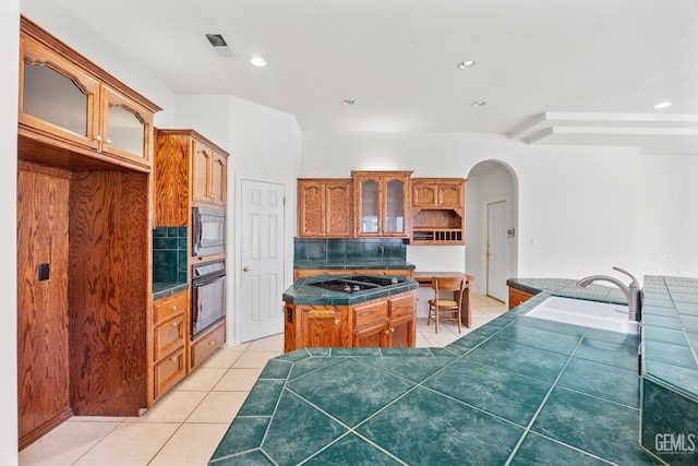 kitchen featuring arched walkways, glass insert cabinets, a kitchen island, black appliances, and tile patterned floors