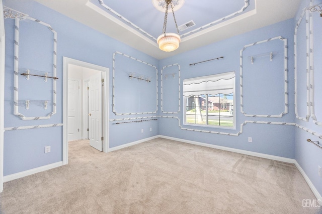 empty room featuring a raised ceiling, light carpet, visible vents, and baseboards