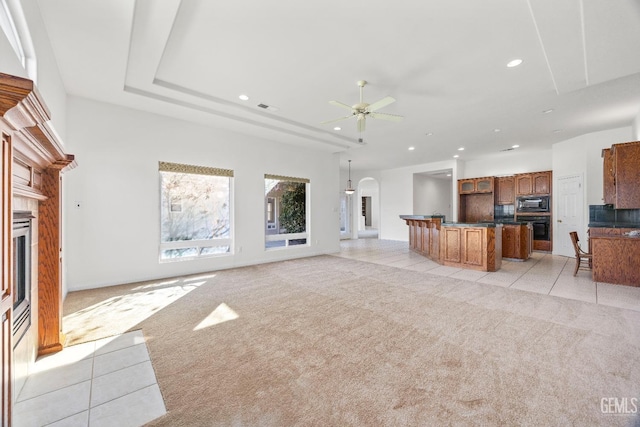 unfurnished living room featuring arched walkways, ceiling fan, recessed lighting, light colored carpet, and a fireplace