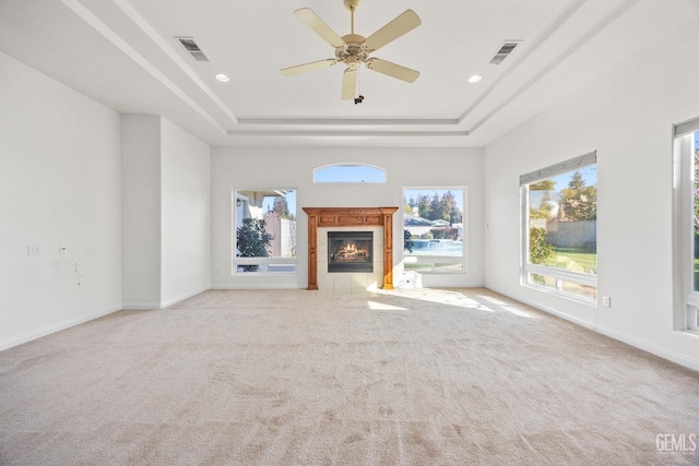 unfurnished living room featuring a tray ceiling, visible vents, and a tiled fireplace