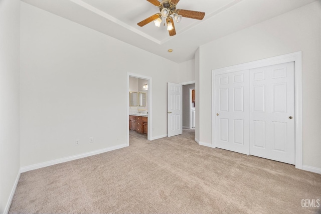 unfurnished bedroom with a closet, light carpet, ensuite bath, and baseboards