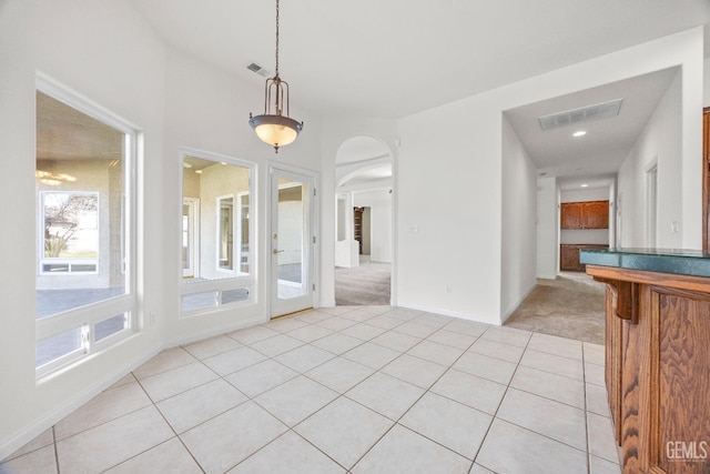 interior space with arched walkways, light tile patterned floors, visible vents, and light colored carpet