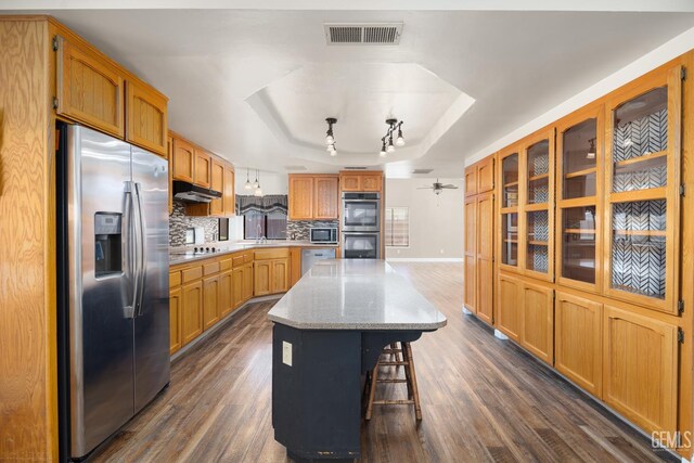 11906 Christy Ave, Bakersfield, CA 93312 - kitchen featuring appliances with stainless steel finishes, a tray ceiling, a center island, dark wood-type flooring, and backsplash