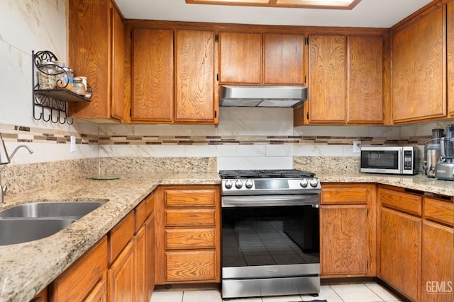 kitchen with sink, light tile patterned floors, appliances with stainless steel finishes, backsplash, and light stone countertops