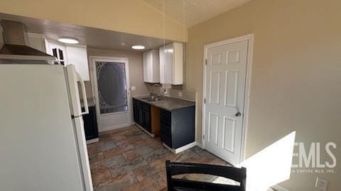 kitchen with vaulted ceiling, white cabinetry, sink, white fridge, and wall chimney exhaust hood