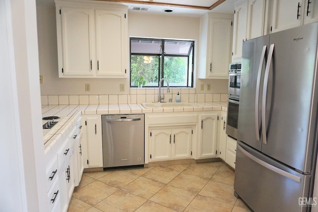 kitchen featuring tile countertops, stainless steel appliances, a sink, visible vents, and white cabinets