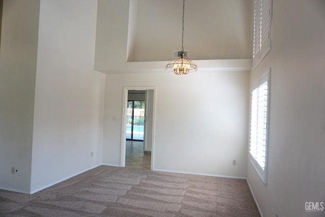 carpeted spare room featuring a towering ceiling, baseboards, and visible vents