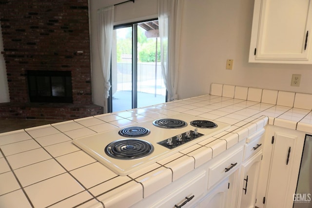 kitchen featuring a peninsula, white cabinets, a brick fireplace, tile counters, and white electric cooktop